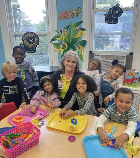 A Little Friends teacher with a smiling group of children at a classroom activity table
