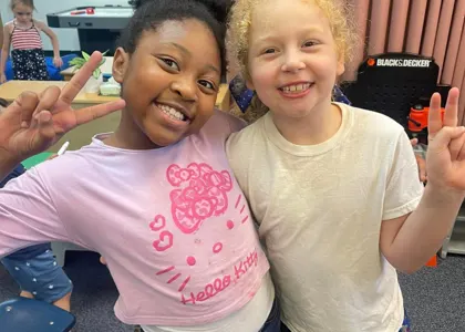 Two smiling classmates posing together in their classroom