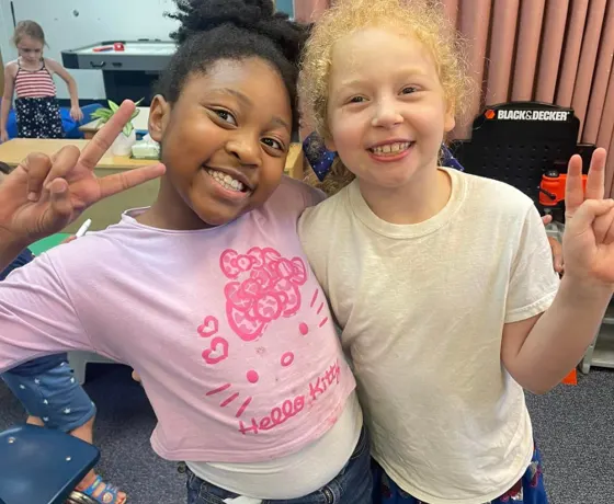 Two smiling classmates posing together in their classroom